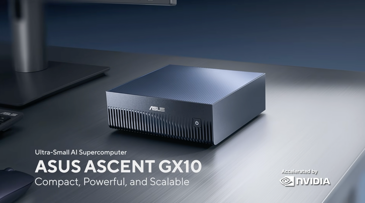ASUS Ascend GX10 ultra-small AI supercomputer shown on a dark desk with a monitor base partially visible. The product is a compact rectangular mini PC with a ribbed front and a metallic dark blue top, with text overlays reading 'Ultra-Small AI Supercomputer ASUS ASCENT GX10 Compact, Powerful, and Scalable' and 'Accelerated by NVIDIA' in the lower right.